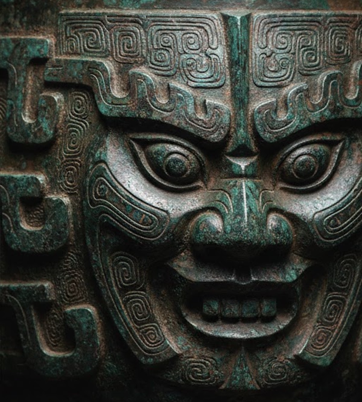 Primer plano de relieve en bronce antiguo con pátina turquesa y detalles de arte histórico oriental.