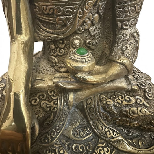 Primer plano de la mano de Buda sosteniendo un cuenco con una piedra verde incrustada.