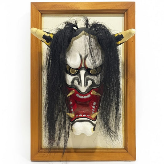 "Vista frontal de máscara japonesa de danza Kagura, representando un demonio Oni con grandes cuernos, expresión feroz, boca abierta con colmillos dorados y cabello largo negro natural. Artesanía tradicional en papel washi sobre marco de madera."